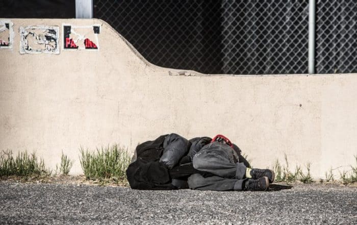 photo of a man covering his head and sleeping in a parking lot